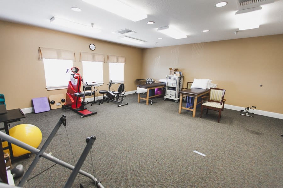 A spacious fitness room equipped with a treadmill and stationary bike, surrounded by chairs.