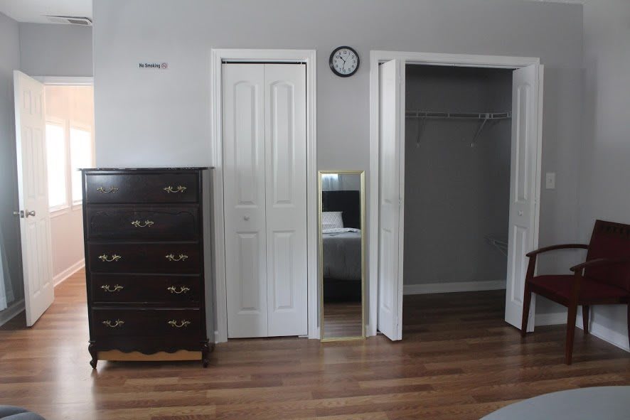 A bedroom with a dresser, mirror, and open closet.