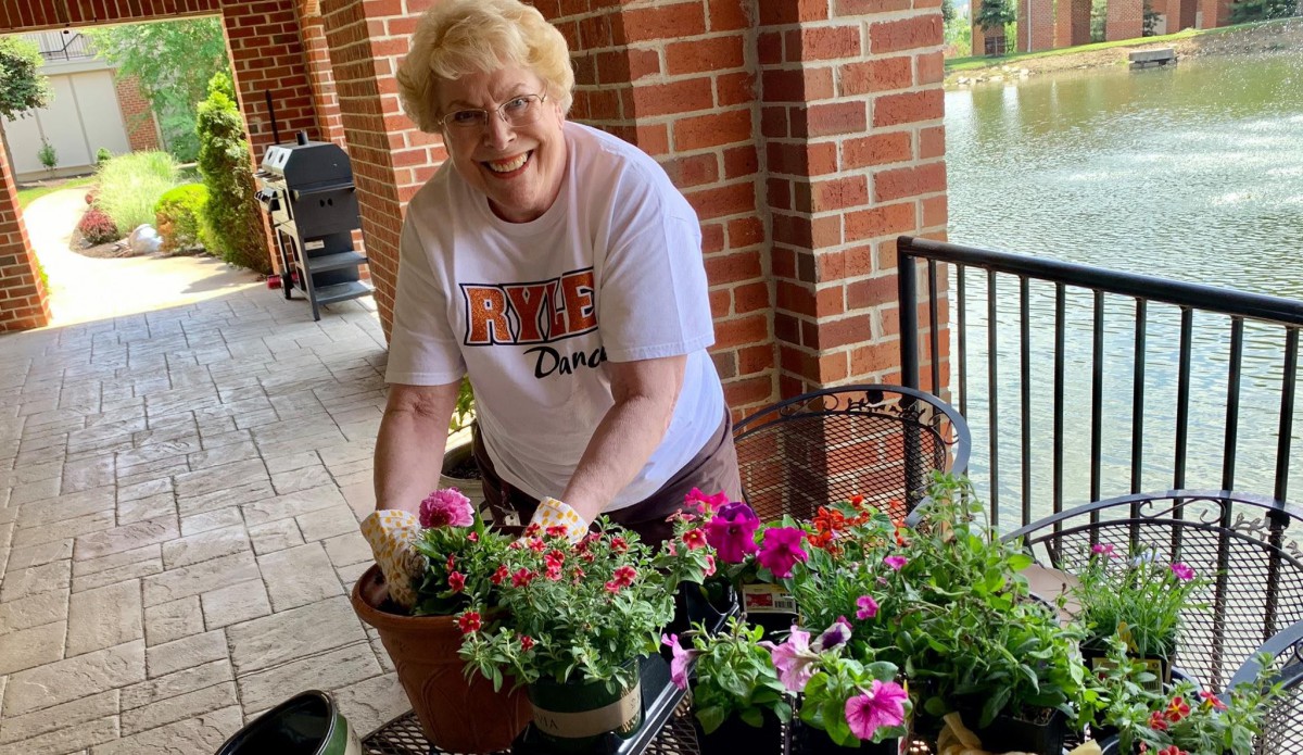 A woman smiles while tending to colorful flowers on a porch.