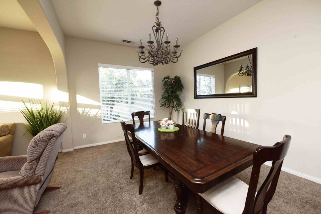 A well-lit dining room featuring a wooden table with six chairs, a chandelier, and a large mirror on the wall.