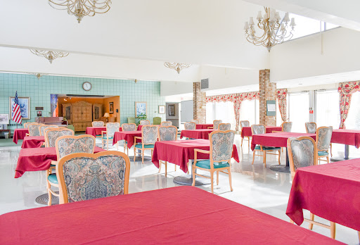 A spacious dining area featuring tables dressed in red tablecloths and elegant chairs, illuminated by a chandelier.