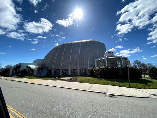 A modern architectural structure under a bright sun and cloudy sky.