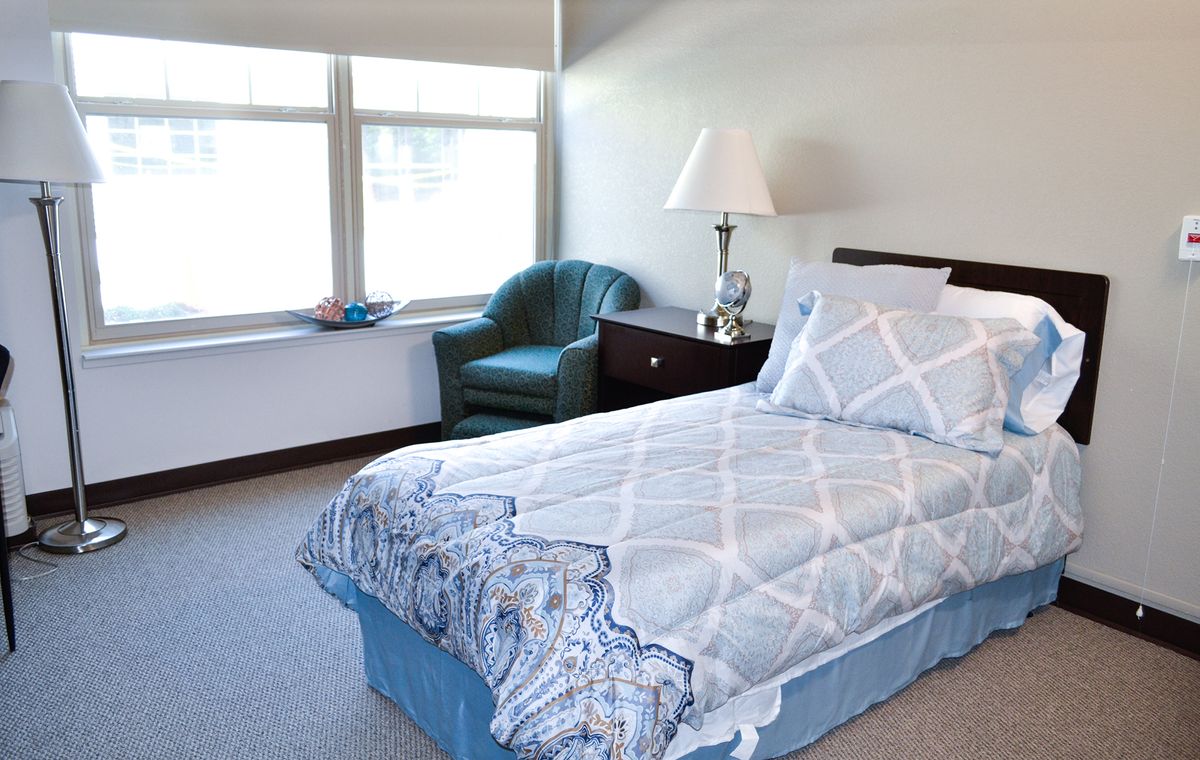 A cozy bedroom with a single bed, lamp, and a chair by the window.