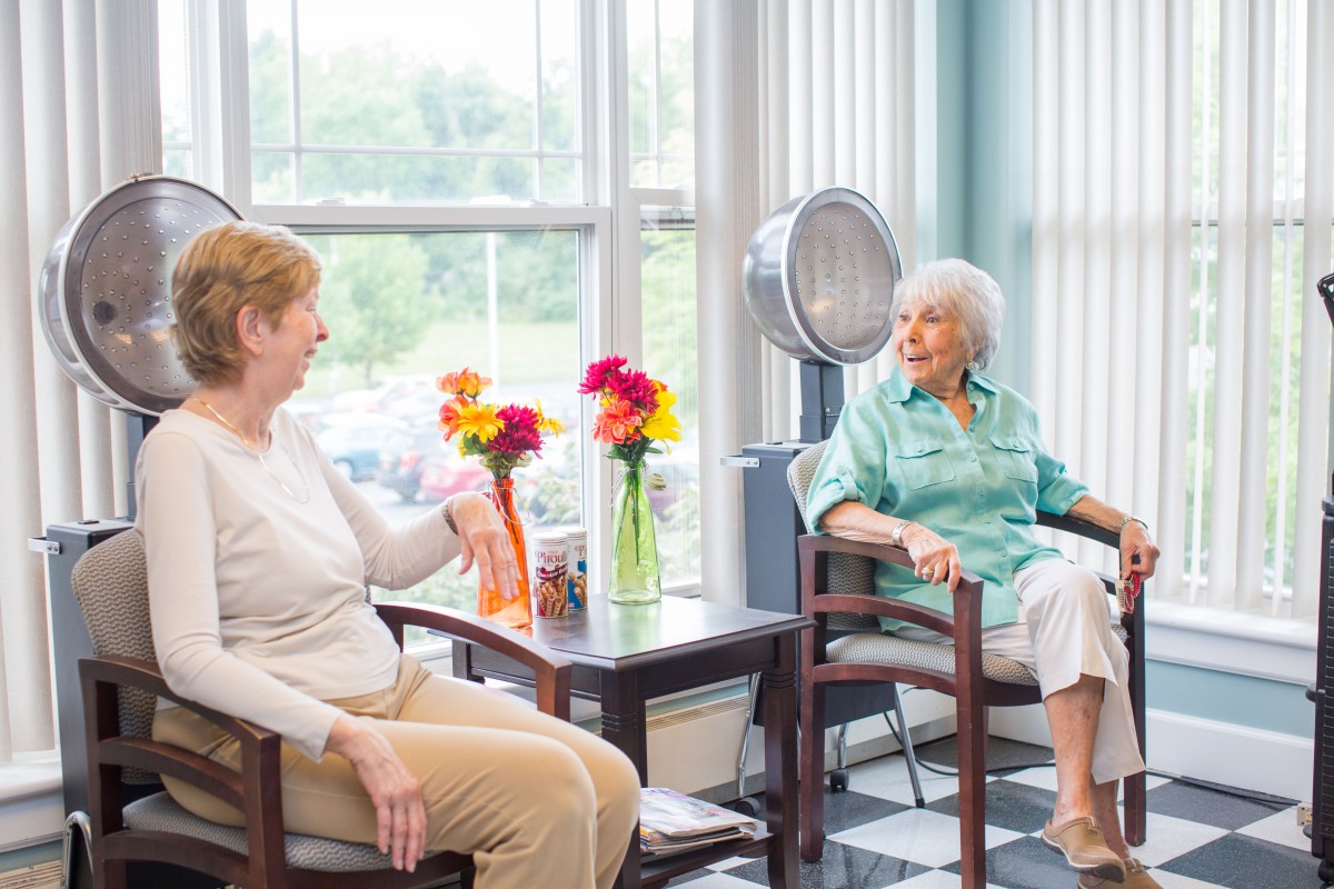 Two elderly women engage in a lively conversation at a hair salon.