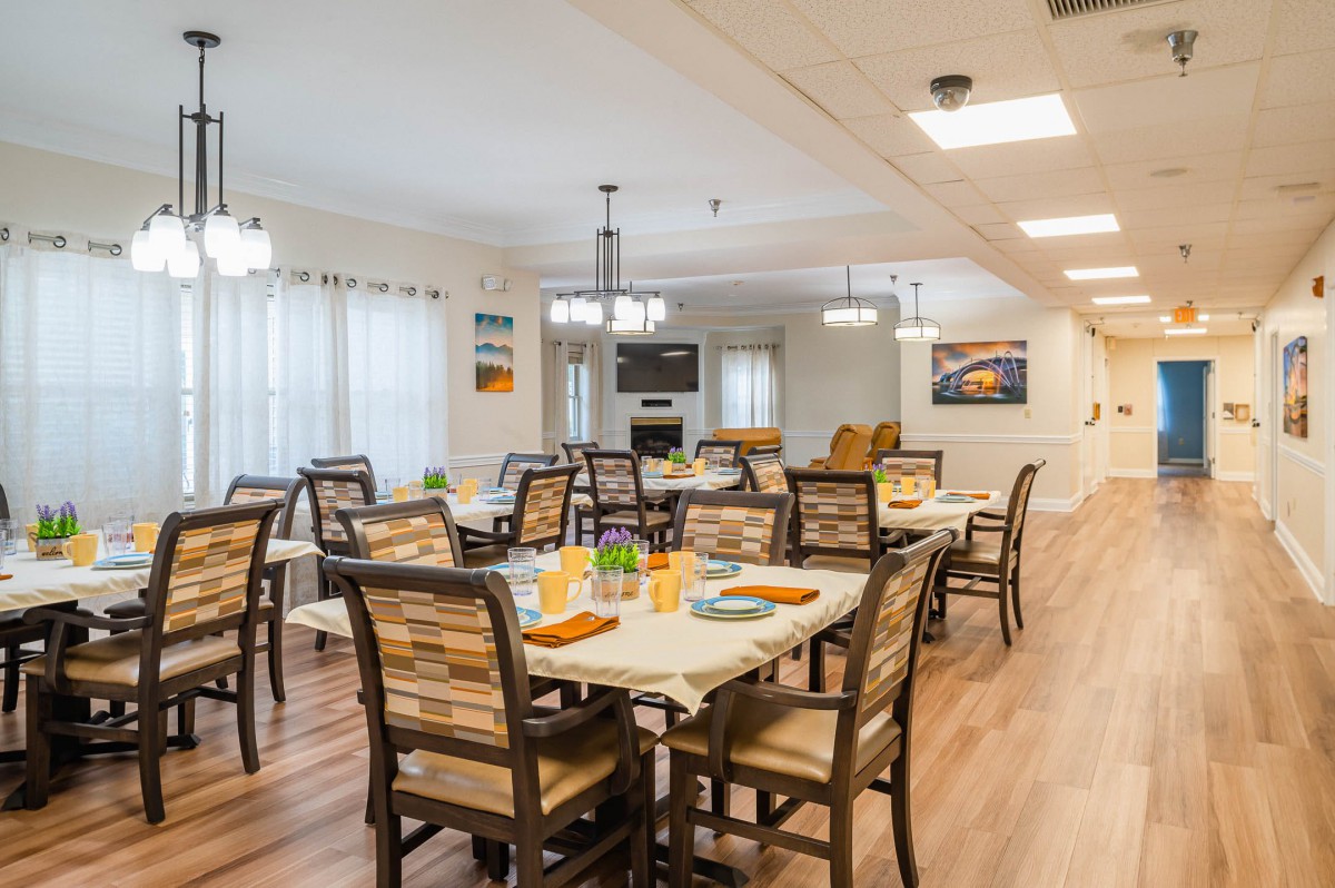 A bright and inviting dining room with neatly arranged tables and chairs, featuring warm decor and ample lighting.