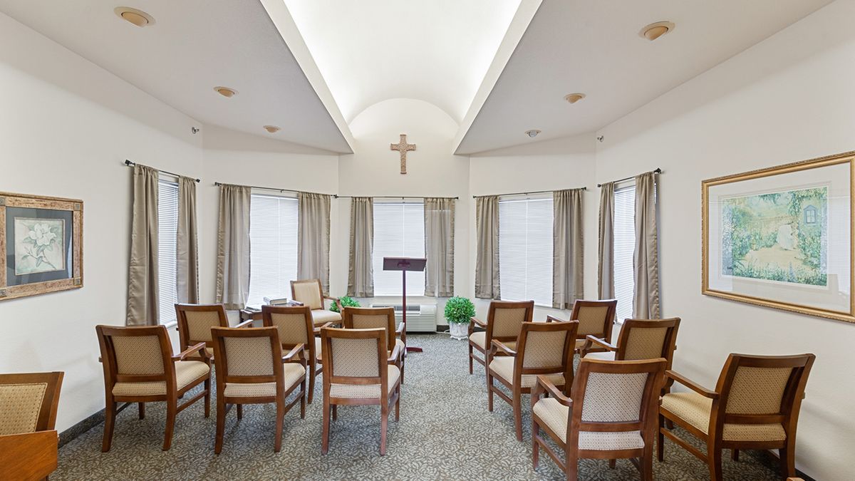 A small chapel interior with chairs arranged in rows, a podium at the front, and a cross on the wall.