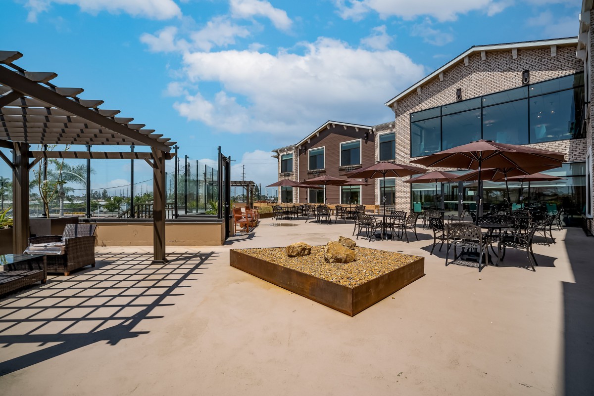 A spacious outdoor patio with ample seating and a sandpit, featuring a modern building under a clear blue sky.