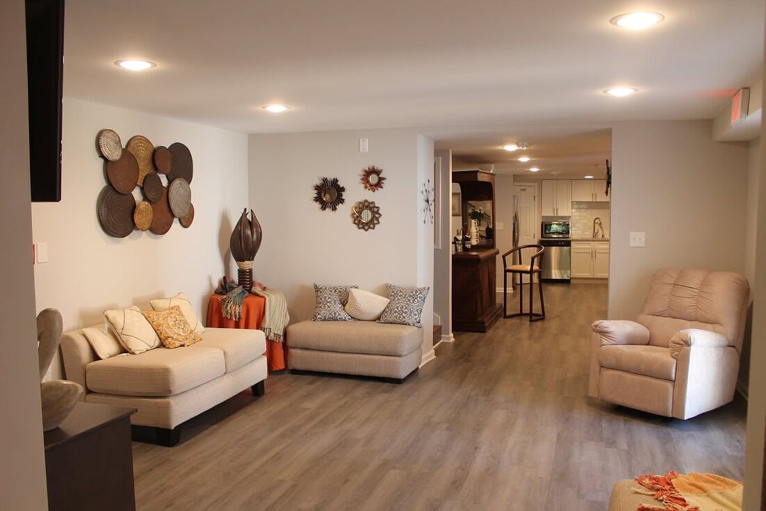 A modern and cozy living room with sofas, decorative items on the wall, and wood flooring leading to an open kitchen area.