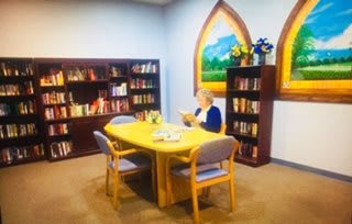 A person reading in a cozy library setting with bookshelves and a table.