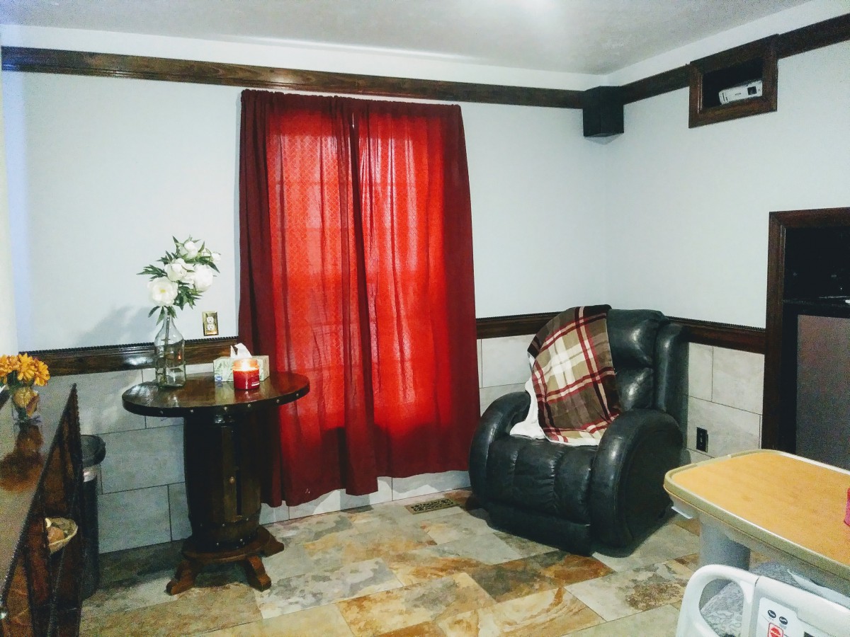 A cozy living room featuring a black armchair, red curtains, and a round table with flowers.