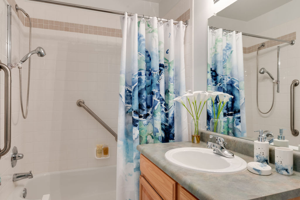 A tidy bathroom featuring a sink with a floral arrangement and a patterned shower curtain.
