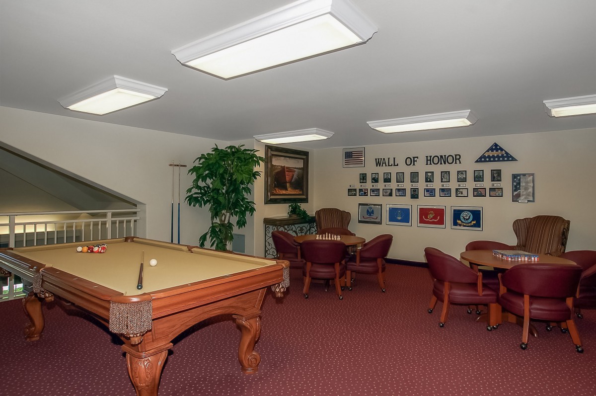 A cozy game room featuring a billiards table and seating area, adorned with a wall of honors and decorative lighting.