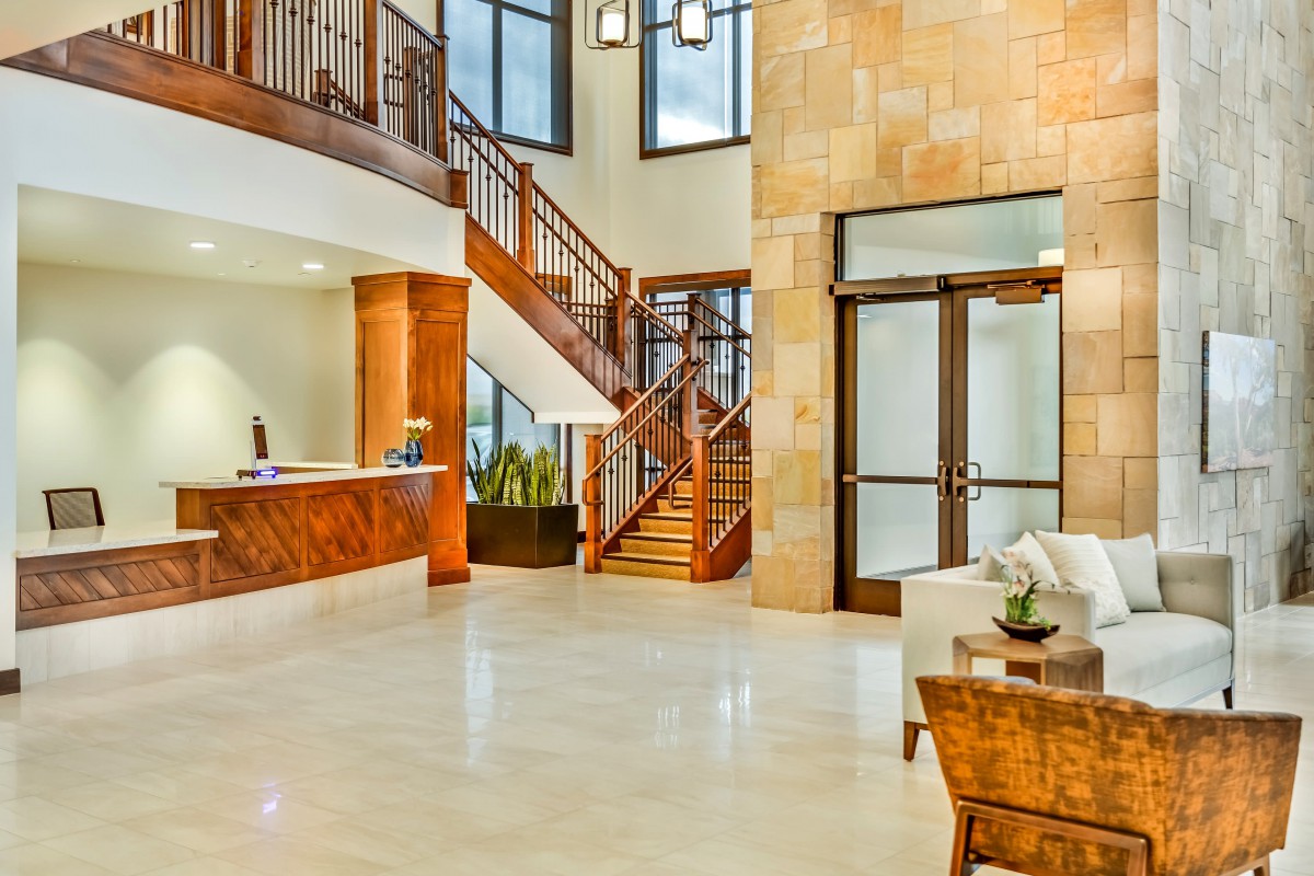 A modern and luxurious lobby featuring a wooden staircase, reception desk, and ample natural light.