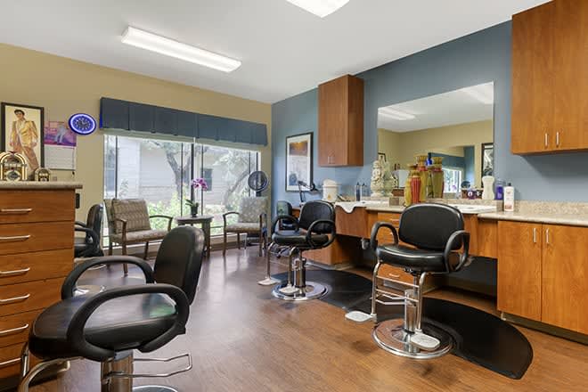 A modern hair salon with styling chairs and a waiting area, featuring large mirrors and wood flooring.
