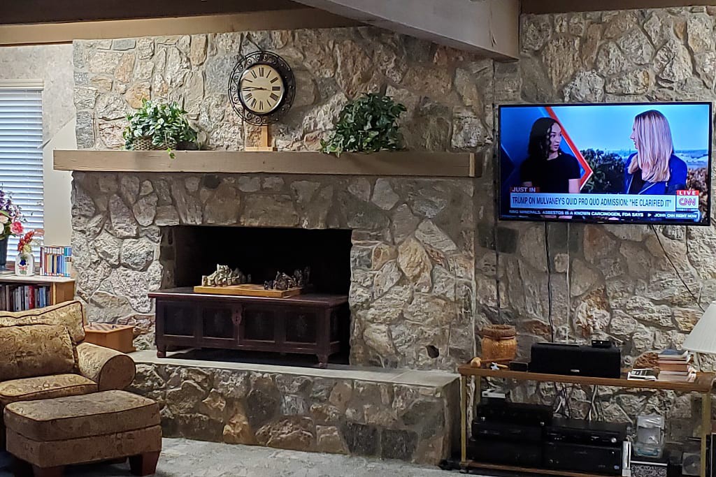 A cozy living room with a stone fireplace and a television mounted on the wall.