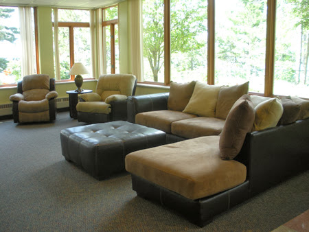 A cozy living room featuring a comfortable sofa, armchairs, and an ottoman, bathed in natural light from large windows.