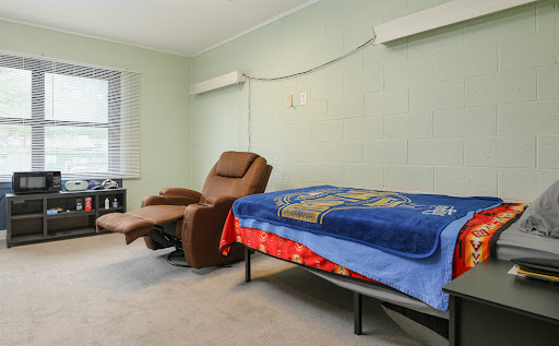 A cozy room featuring a recliner and a bed, adorned with a colorful blanket.