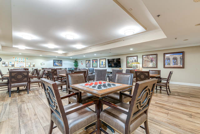 A spacious dining or activity area featuring several tables and chairs, with a checkers board on one table and framed artwork on the walls.