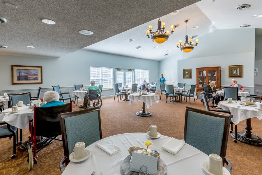 A spacious dining room with neatly arranged tables and chairs, featuring chandeliers and large windows.