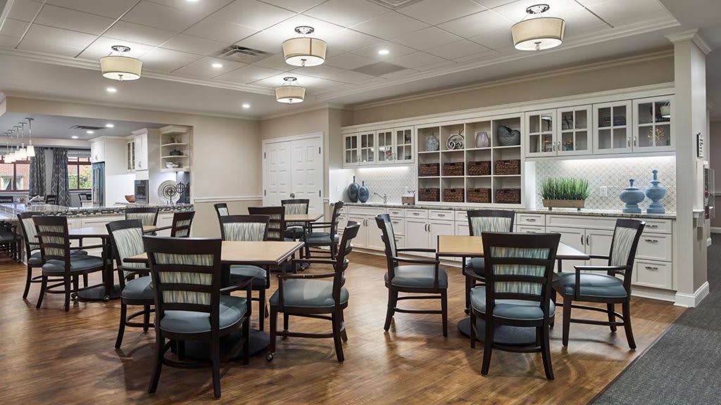 A well-lit dining room with multiple tables and chairs, featuring elegant cabinetry and wooden flooring.