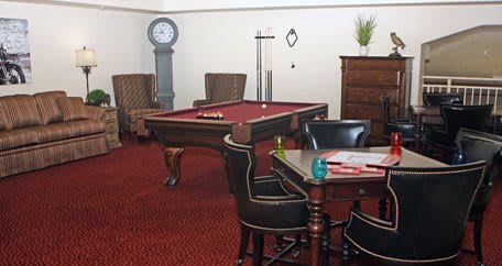 A cozy game room featuring a billiard table, chairs, and a standing clock on a carpeted floor.
