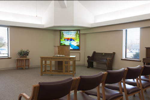 A peaceful chapel interior featuring wooden furniture and a vibrant presentation screen.