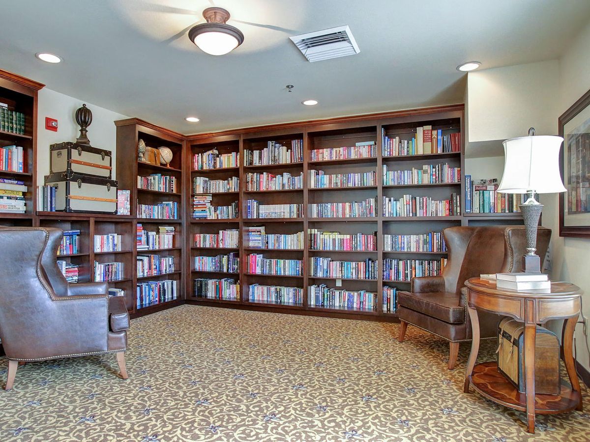 A cozy library room with wooden bookshelves filled with books, an armchair, and a ceiling fan.
