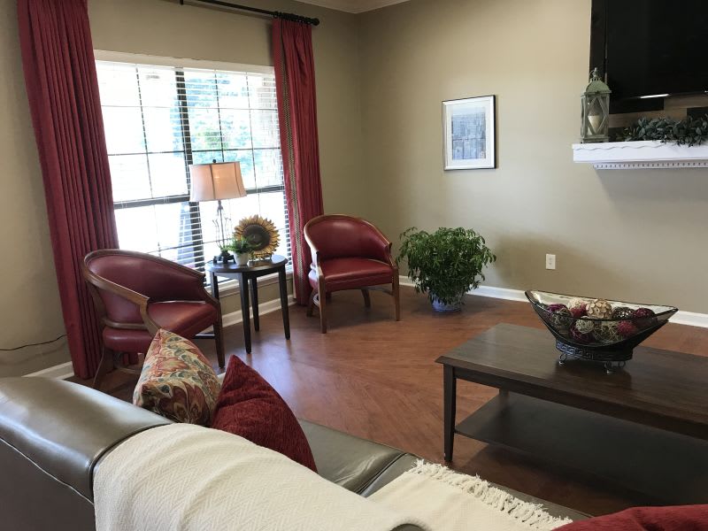 A cozy living room with elegant red chairs, a coffee table, and natural lighting from a large window.