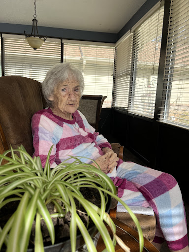 An elderly woman relaxes in her cozy indoor space, dressed in comfortable plaid pajamas.