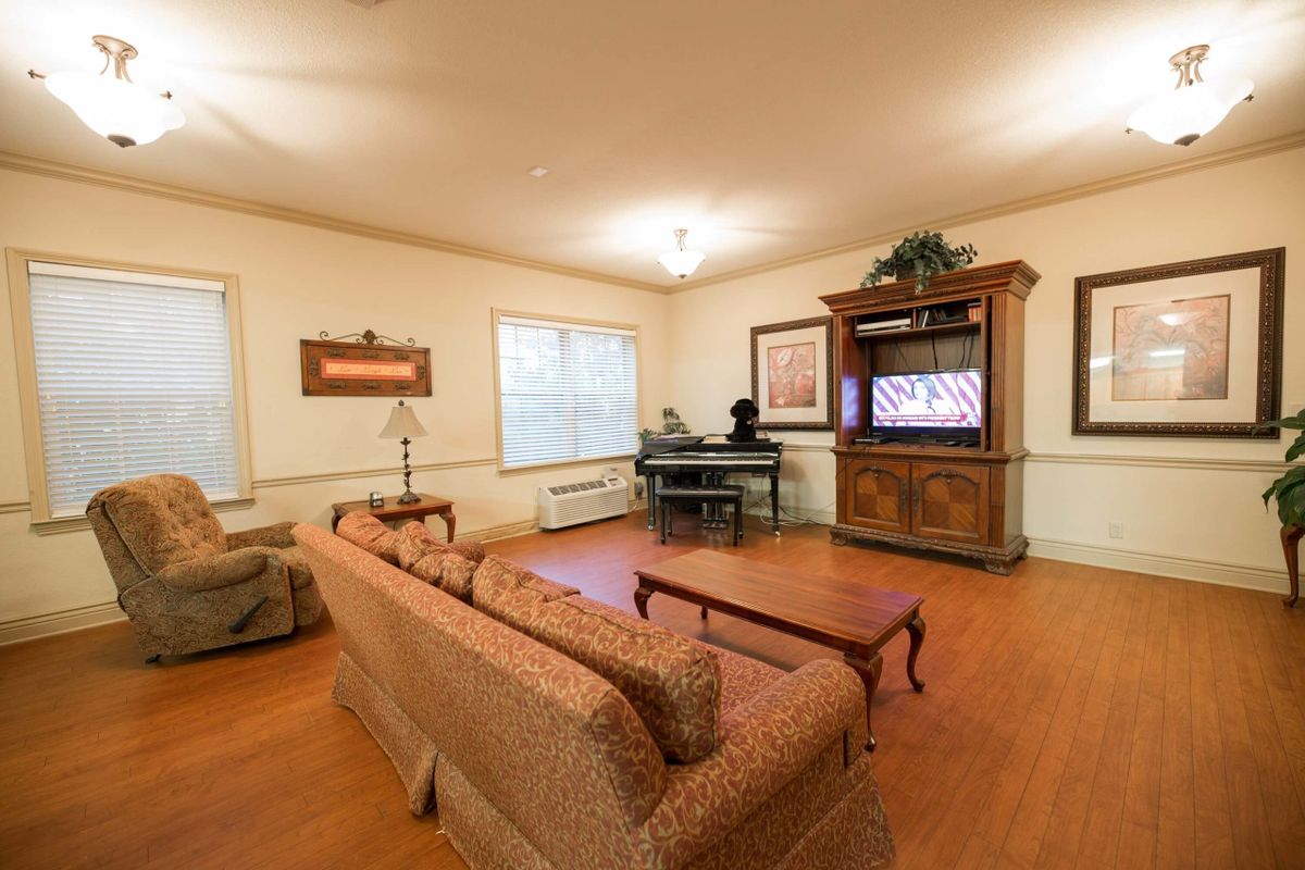 A cozy living room featuring a sofa, piano, and television with wooden flooring.
