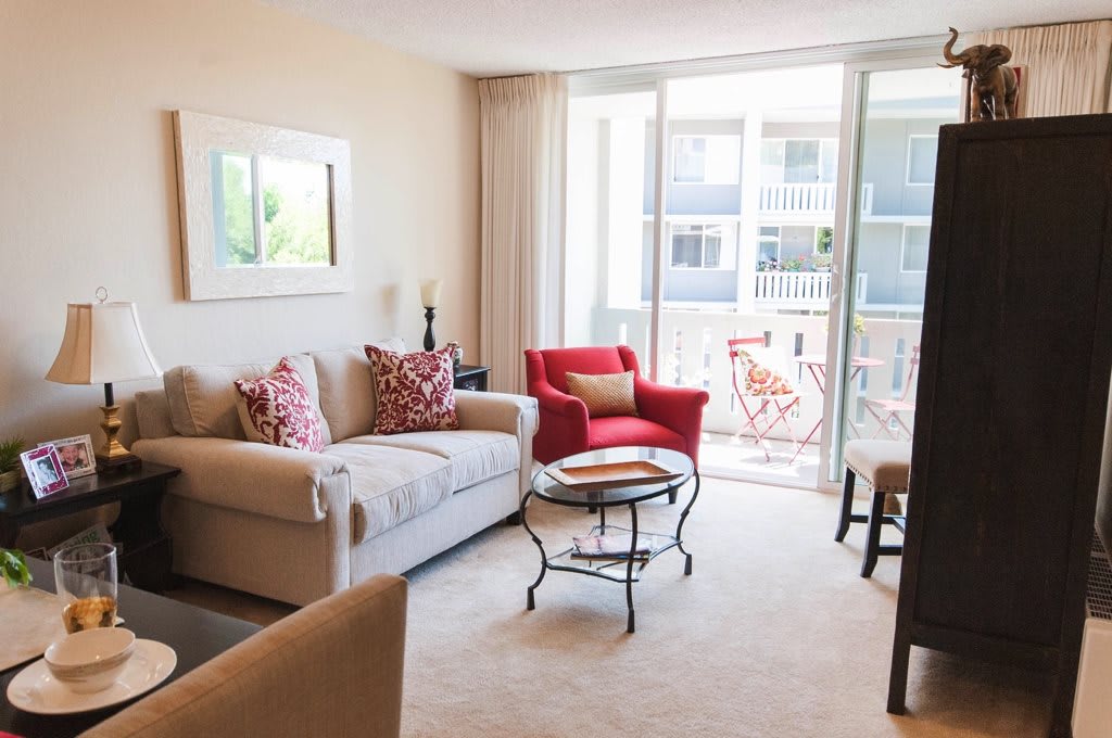 A bright and inviting living room with a comfortable sofa, red armchair, and coffee table overlooking a balcony.