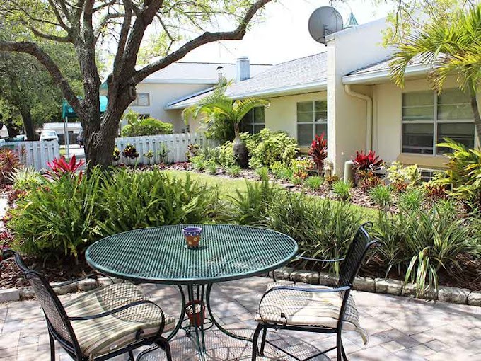 A serene backyard patio with a glass table and chairs surrounded by lush landscaping.