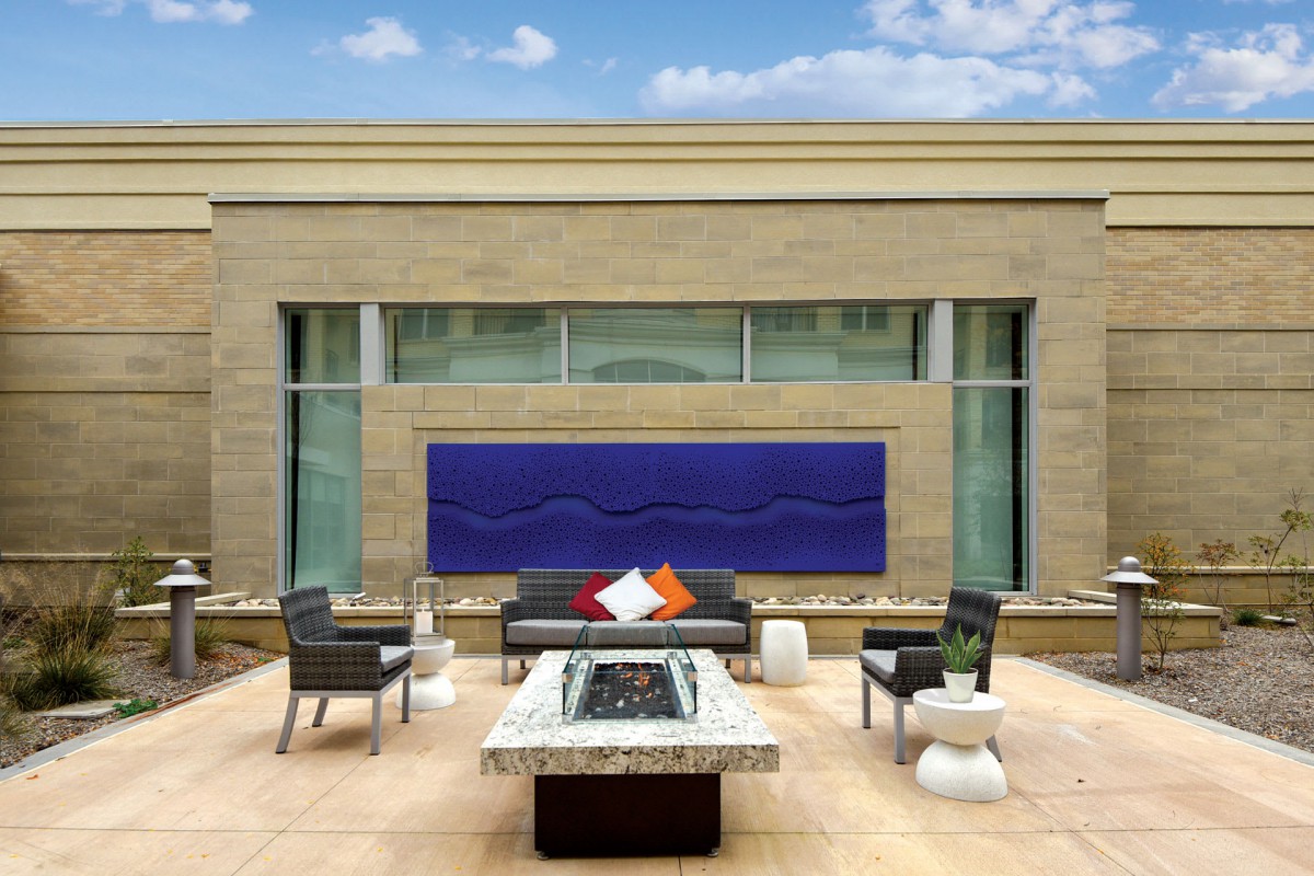 A modern outdoor patio with stylish furniture and a fire pit, framed by a large piece of wall art.