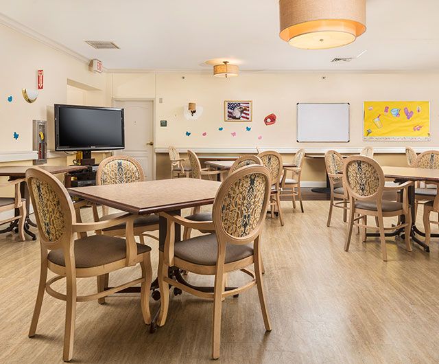 A cozy dining area with neatly arranged tables and chairs, featuring a wall-mounted television and decorative elements.