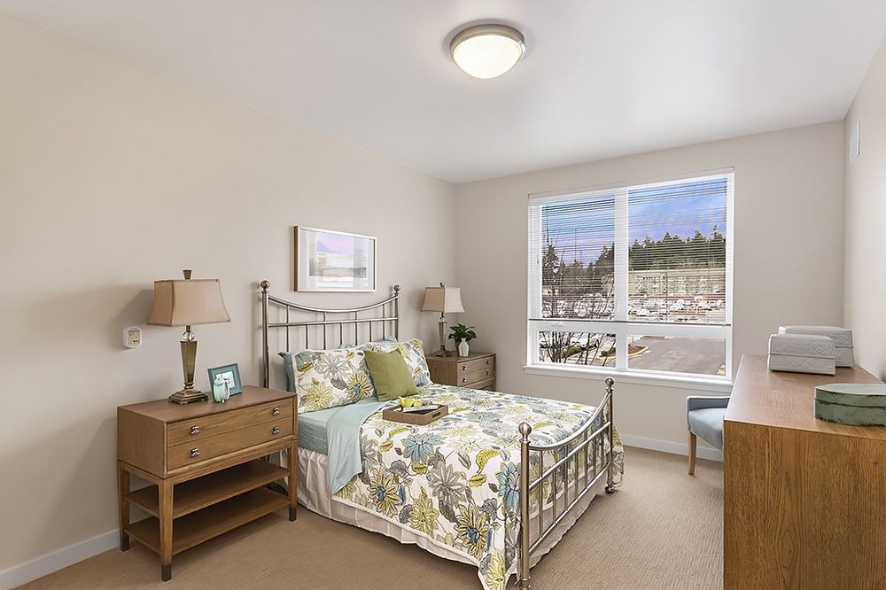 A cozy and well-lit bedroom with a floral-themed bedspread and wooden furniture.