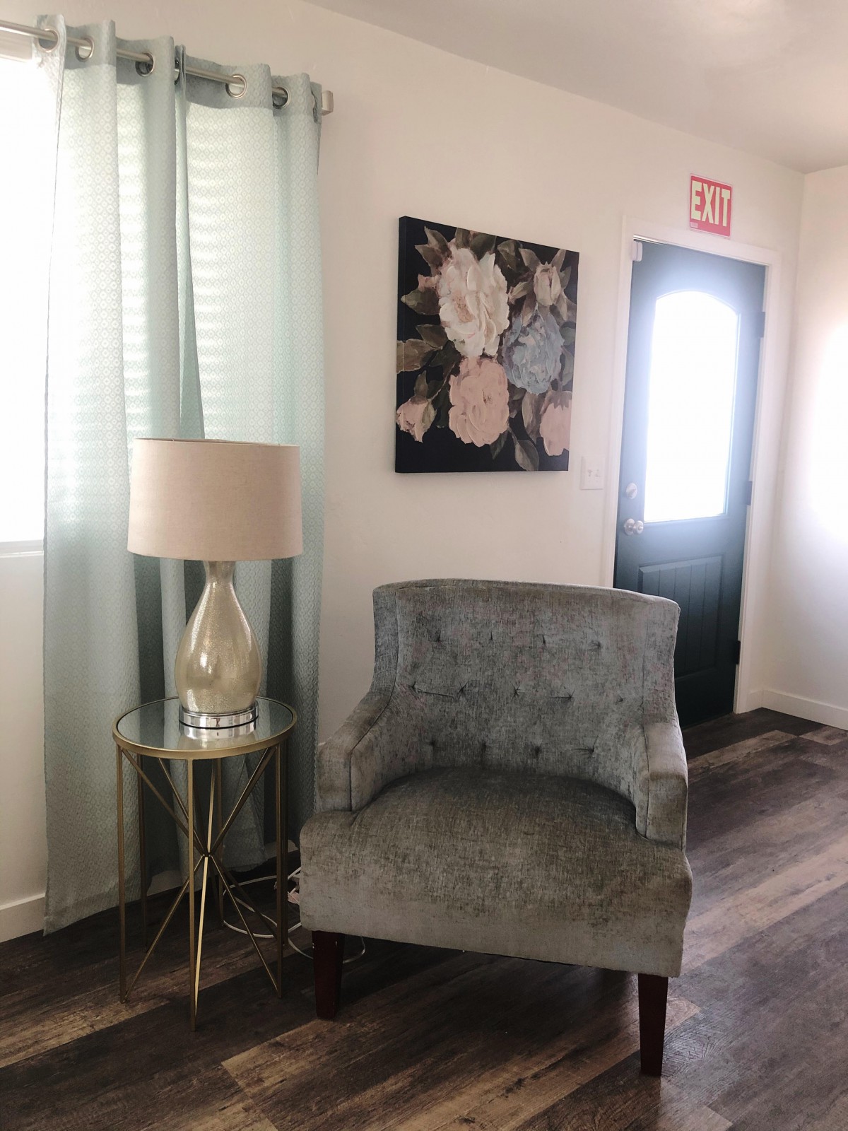 A cozy living space featuring a plush chair, a small side table with a lamp, and floral artwork on the wall.