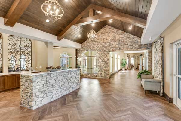 A spacious reception area featuring a wooden ceiling, stone walls, and elegant chandeliers above herringbone flooring.