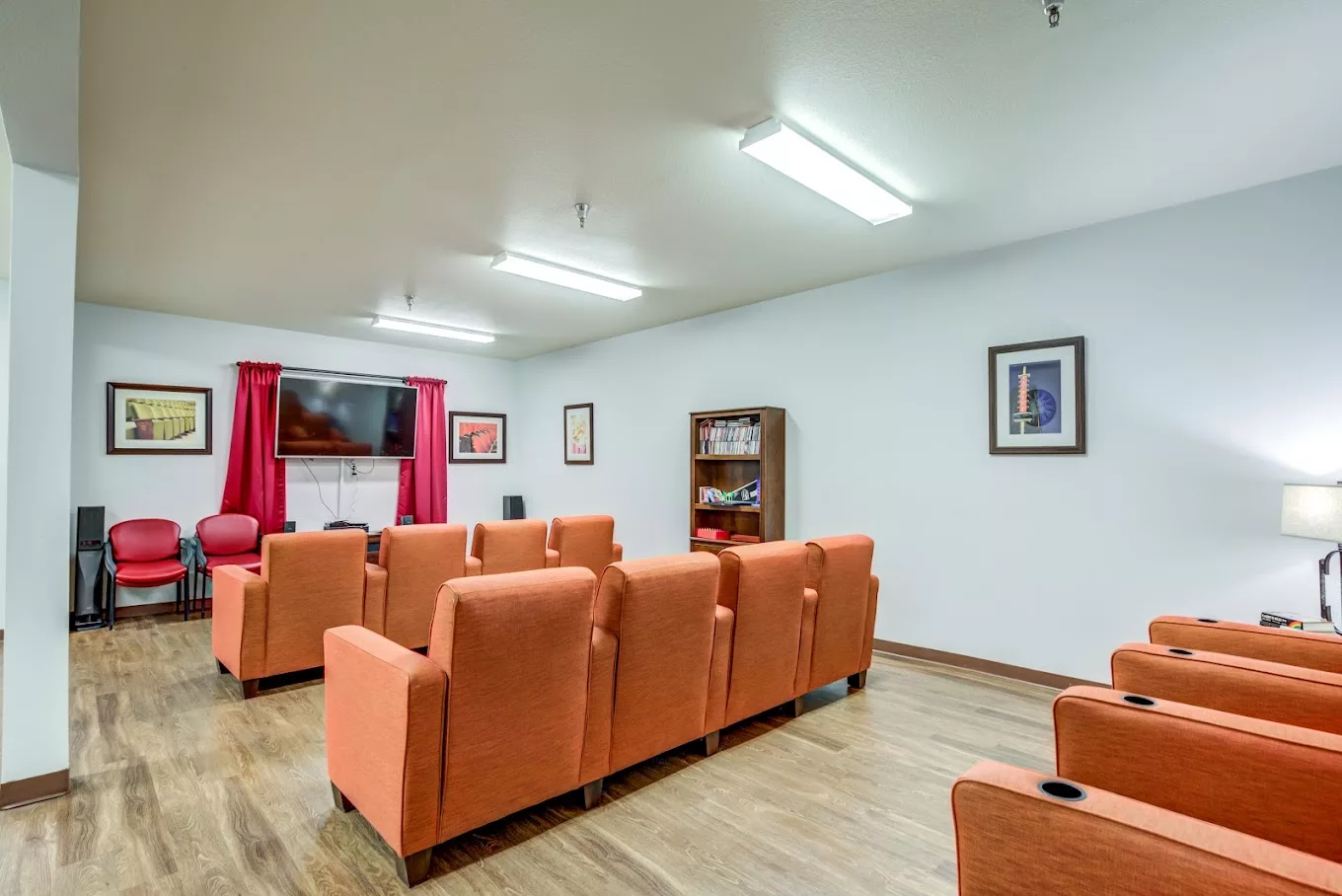 A cozy lounge area with orange chairs facing a television and decorated with artwork on the walls.