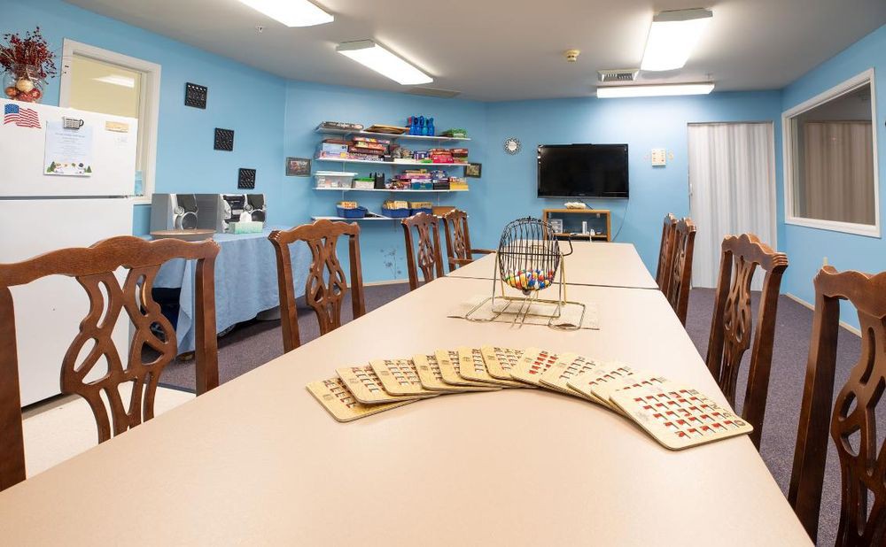 A recreation room set up for a bingo game, featuring blue walls, a long table with chairs, and a television.