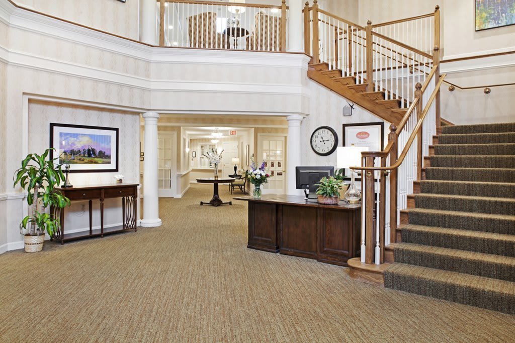 A spacious lobby featuring a wooden staircase, reception desk, and elegant decor.