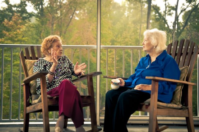 Two elderly women engaged in conversation while sitting on a porch.