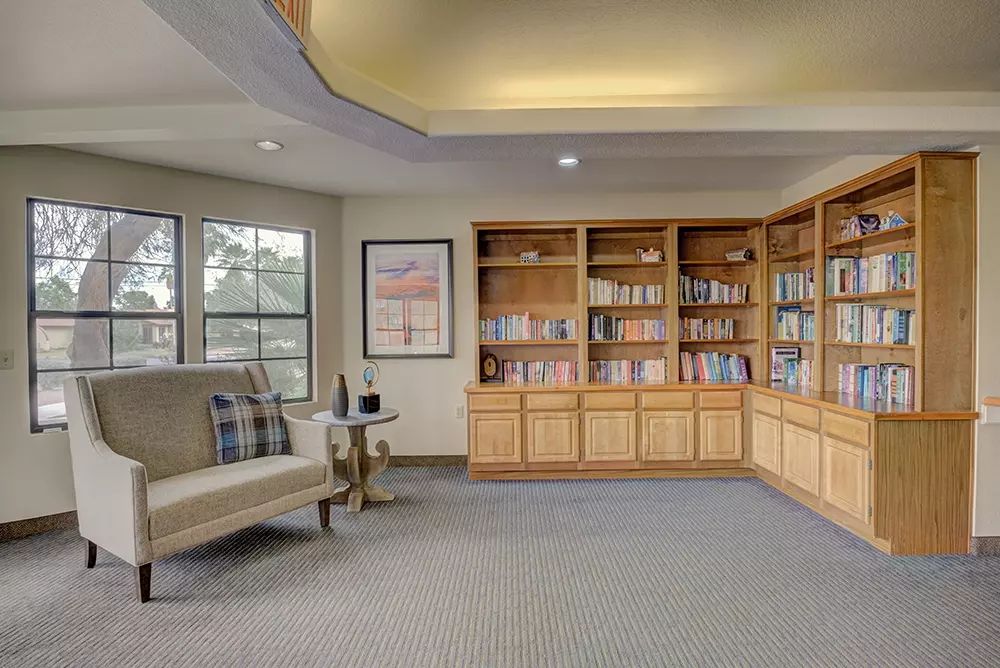 A cozy library room with wooden bookshelves, a comfortable seating area, and large windows.