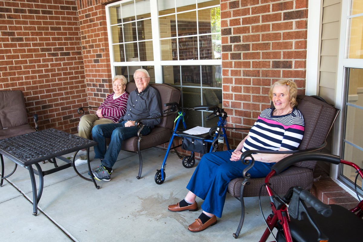 A group of seniors sitting on a porch with walkers nearby.