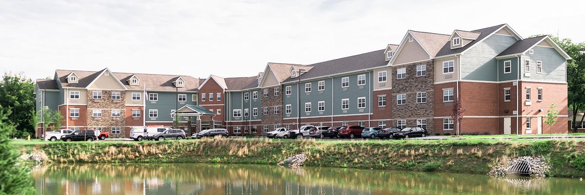 A residential building with a parking lot and a lake in the foreground.