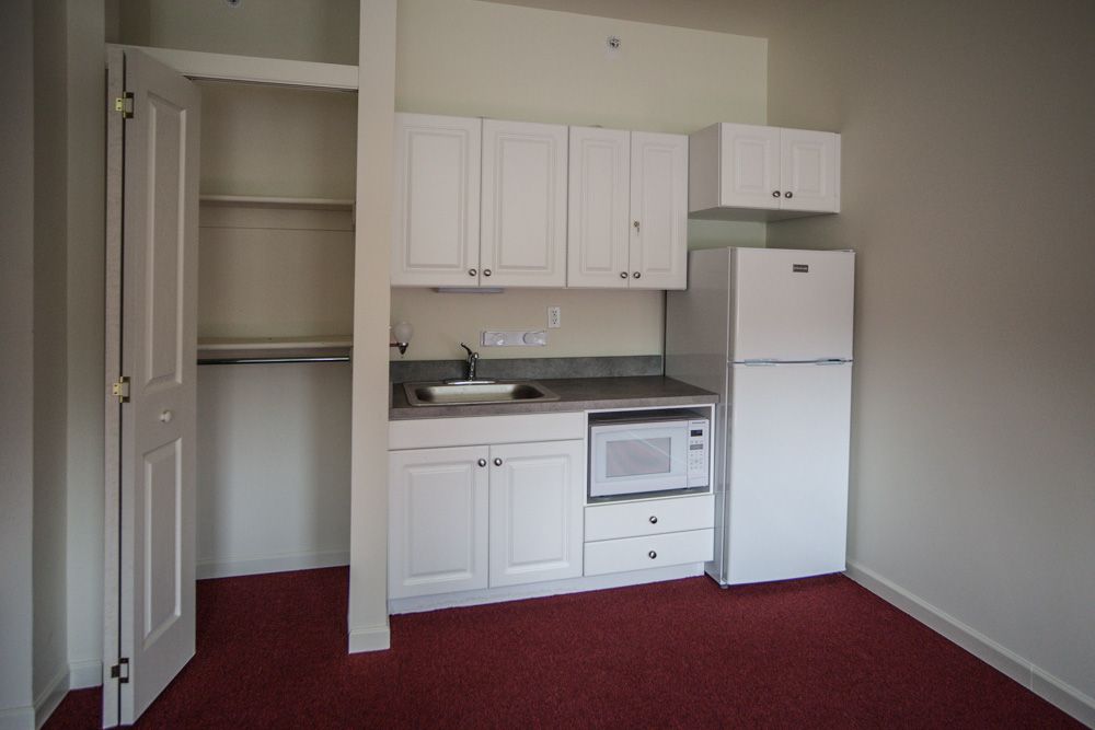 Compact kitchenette with white cabinets and appliances in an apartment.