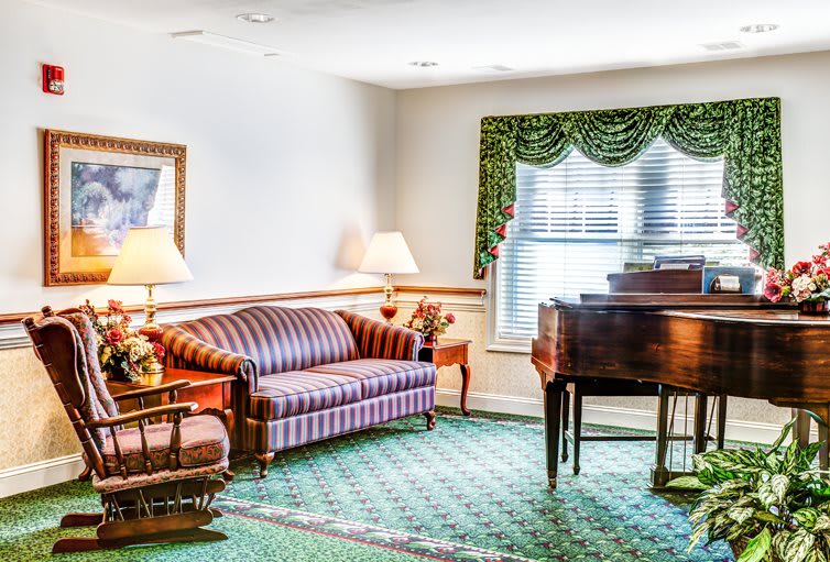 A cozy living room featuring a striped sofa, a grand piano, and two lamps next to a window with green curtains.