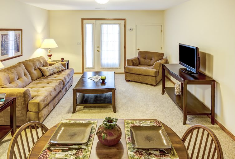 Cozy living room with a sofa, armchair, and a TV, featuring a dining area in the foreground.