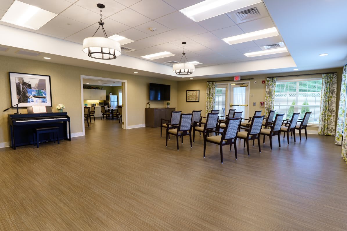 A spacious meeting room with arranged chairs, wood flooring, and ample lighting.