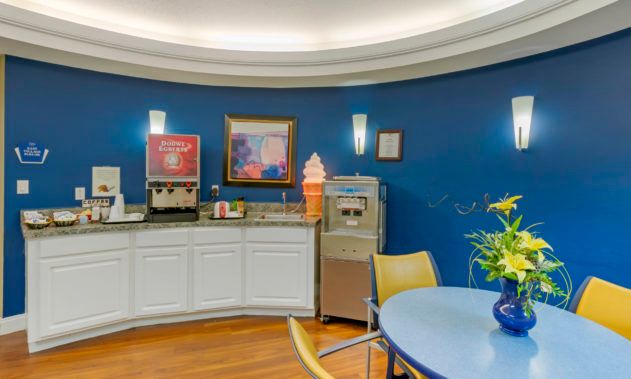 A cozy cafe corner featuring an ice cream machine and beverage dispenser against blue walls.