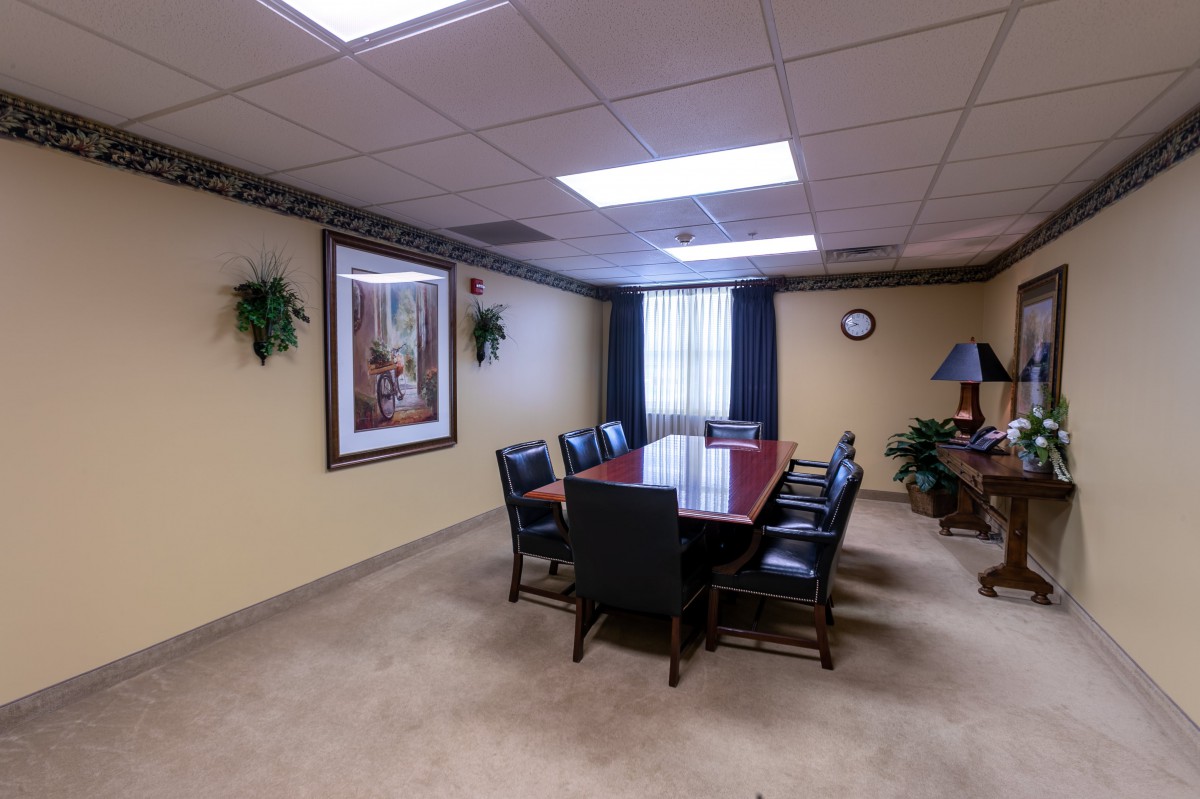 A neatly arranged conference room with a large table and chairs, decorated with artwork and plants.
